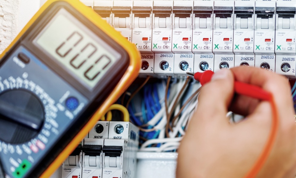 An electrical contractor uses a multimeter to test circuits in an electrical supply panel.