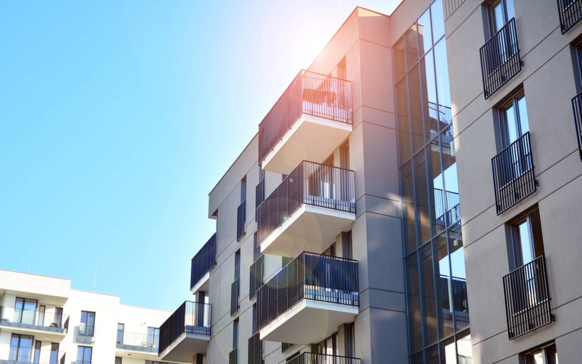 Sunlight illuminates the modern exterior of a multifamily apartment building, highlighting the balconies and windows, ideal for showcasing property management supplies.